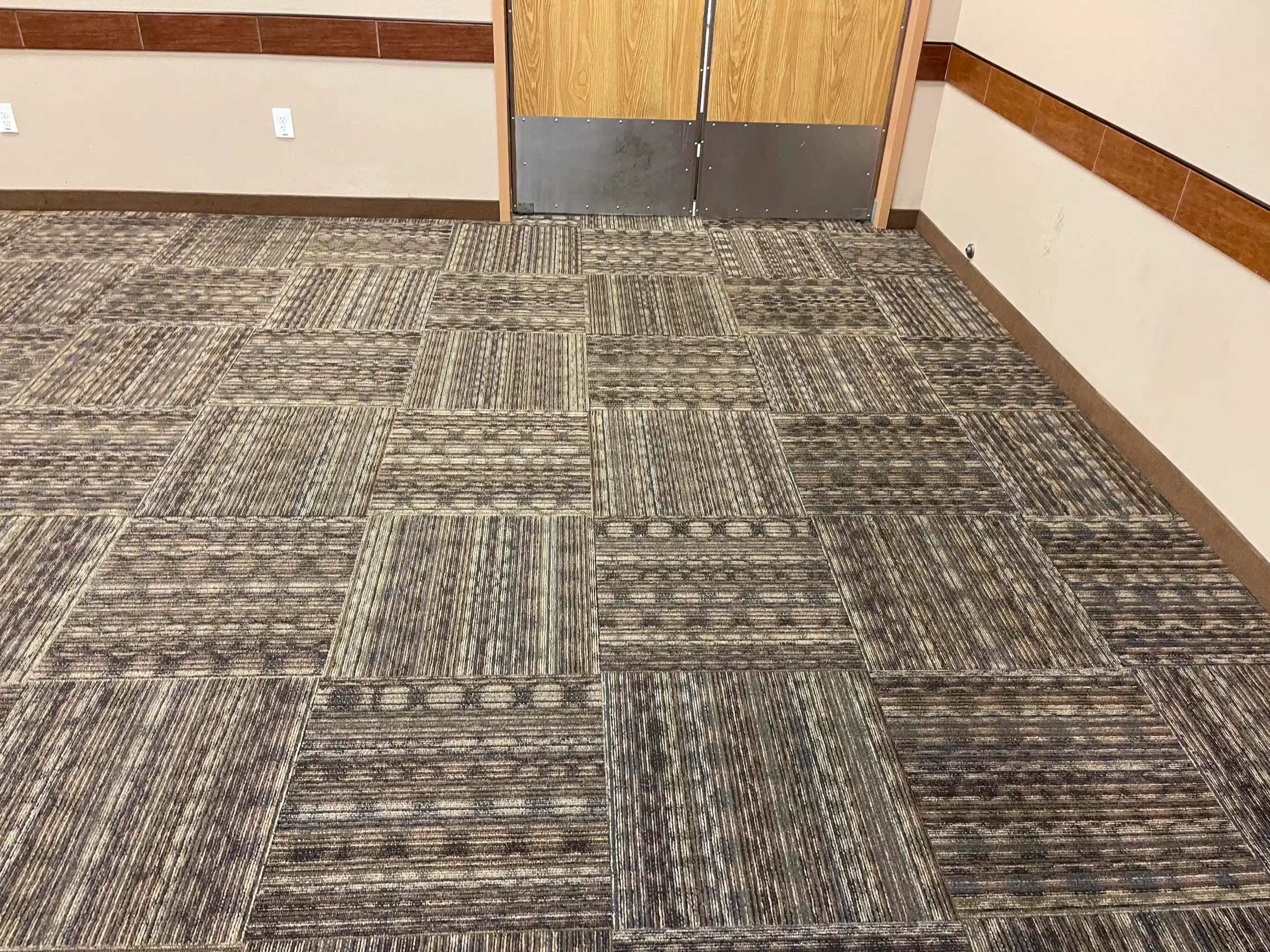 Dirty commercial carpet with visible stains and heavy wear in a high-traffic area, featuring square patterned tiles.